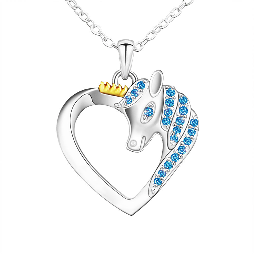 A silver pendant in the shape of a heart with a crown-wearing unicorn figure in the center, surrounded by small blue  stones.