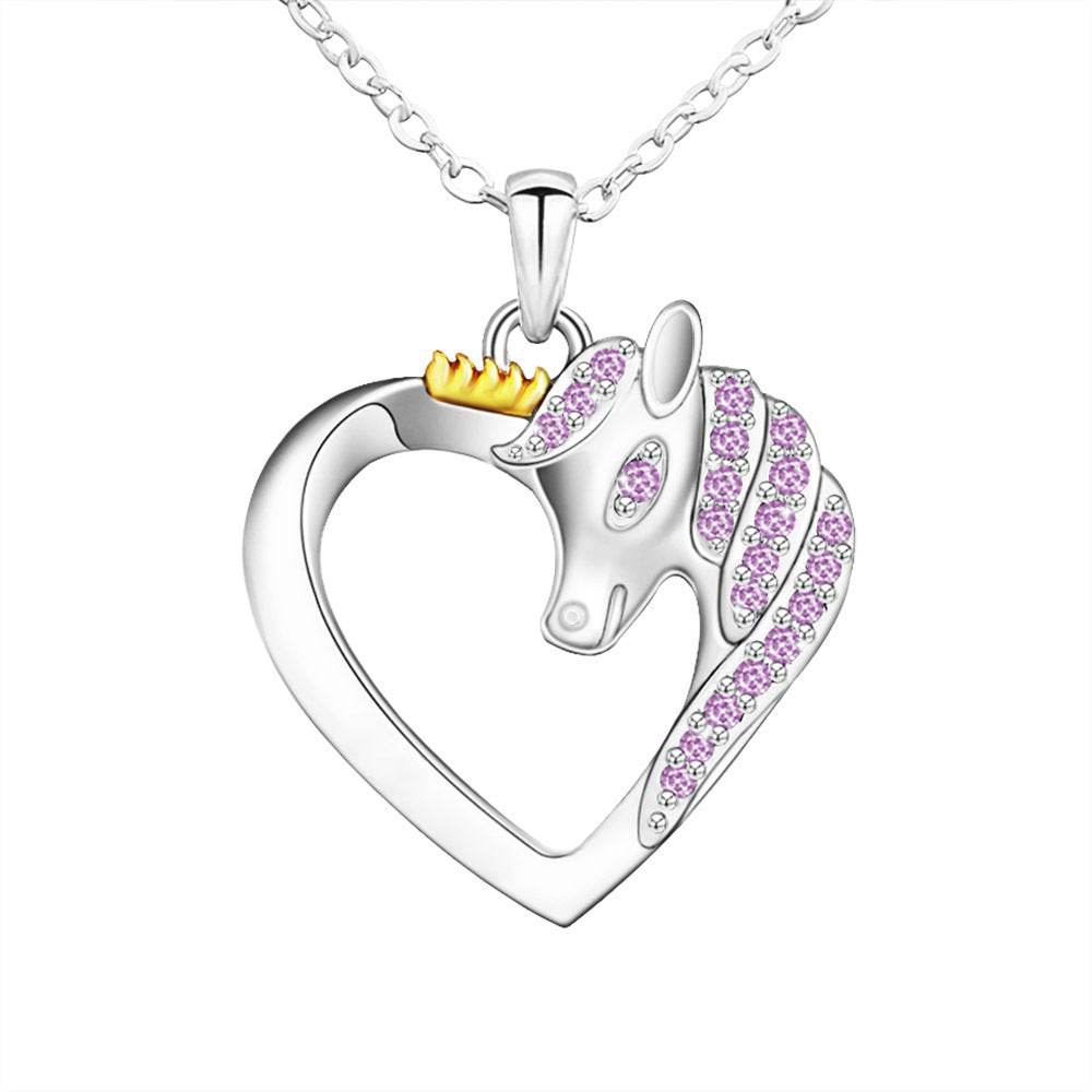 A silver pendant in the shape of a heart with a crown-wearing unicorn figure in the center, surrounded by small purple and pink stones.
