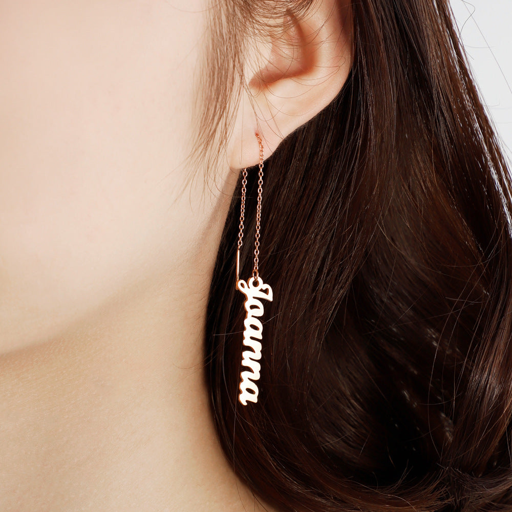 A person wearing a pair of silver long chain earrings with the word 'Guana' inscribed on the chain.
