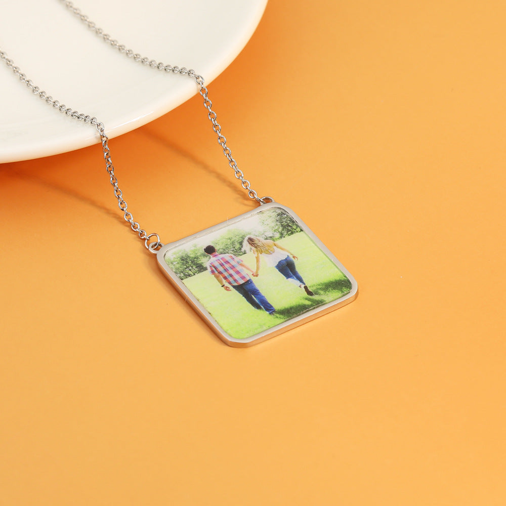 A square-shaped titanium steel necklace pendant with a photo of two people in a park on an orange background, attached to a silver chain.