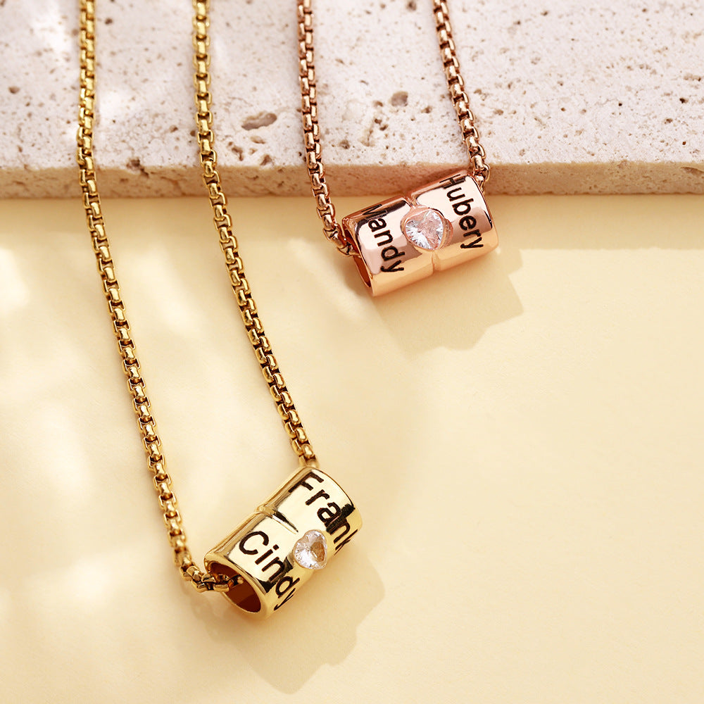 Two gold-colored necklaces with rose gold pendants, one larger and one smaller, each with an engraved name on it, displayed on a reflective surface.