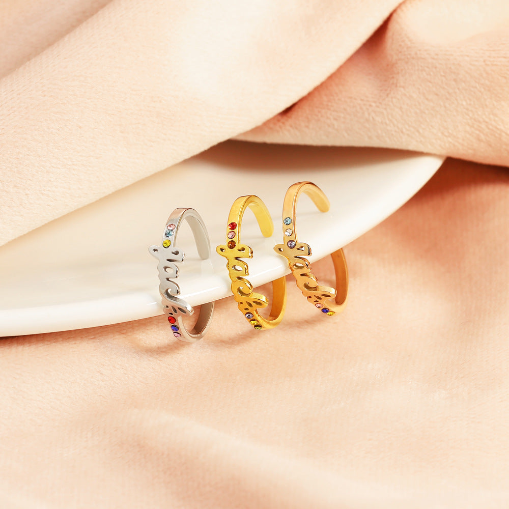 Three rings with gold and silver colors and adorned with red and multicolored gemstones placed on a pale pink fabric surface.