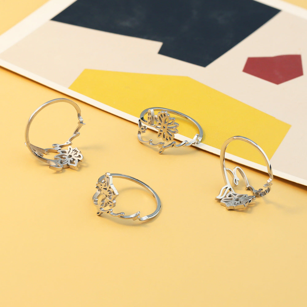 A stainless steel ring with a floral design, placed on a silky fabric surface.