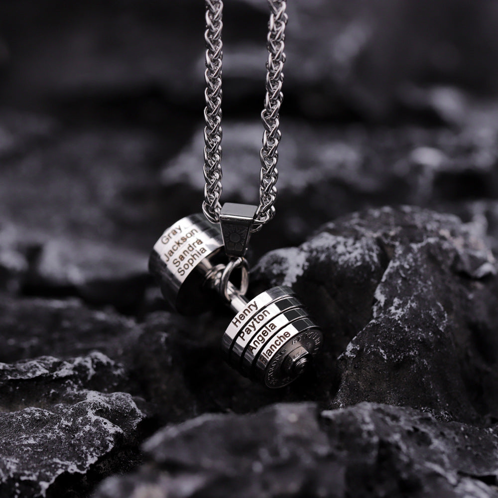 A stainless steel dumbbell-shaped necklace pendant with a chain, resting on a textured dark surface.