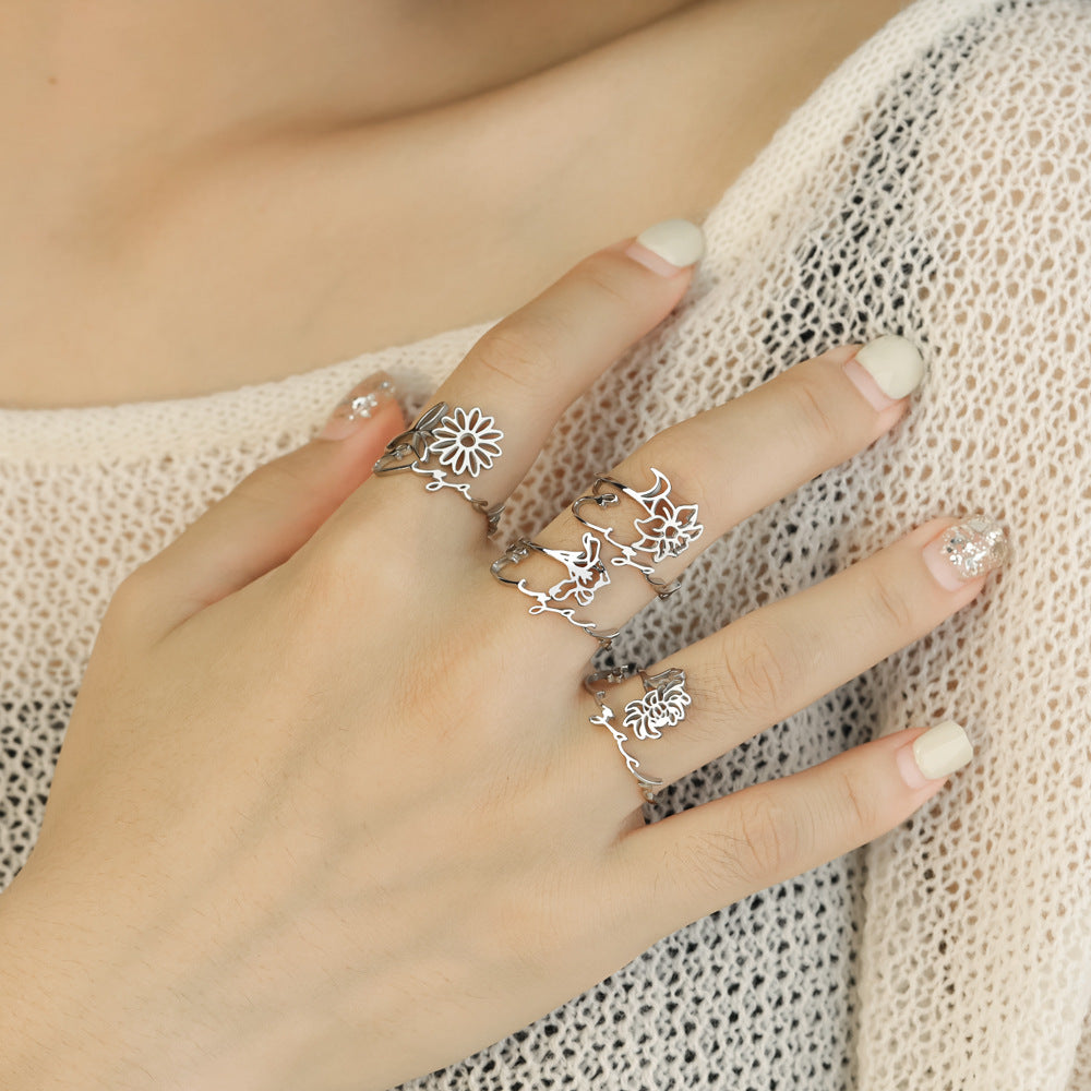 A stainless steel ring with a floral design, placed on a silky fabric surface.