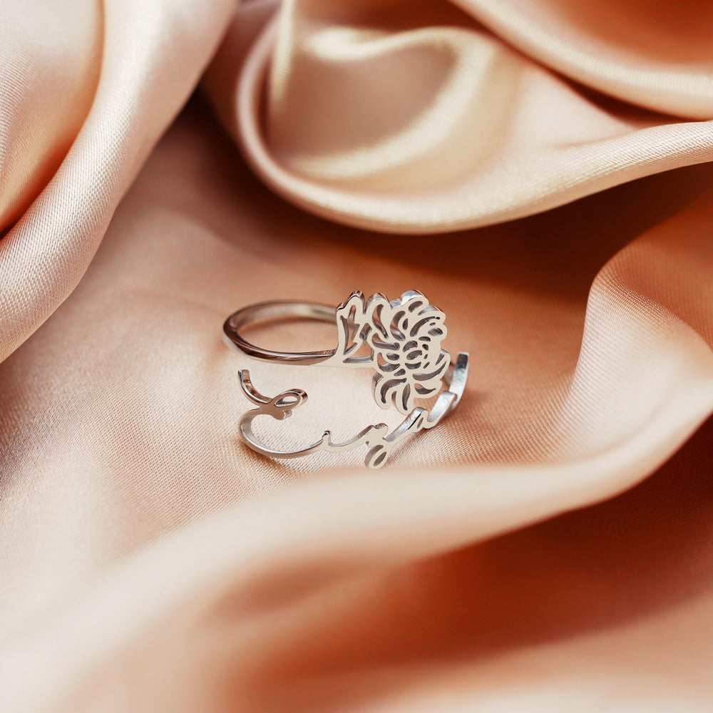 A stainless steel ring with a floral design, placed on a silky fabric surface.