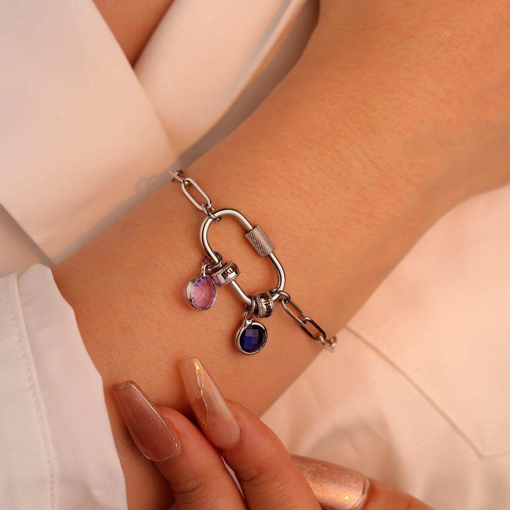 A two-part jewelry set with a pendant and a bracelet, featuring colorful gemstones and metallic clasps, displayed on a surface with pink crystals.