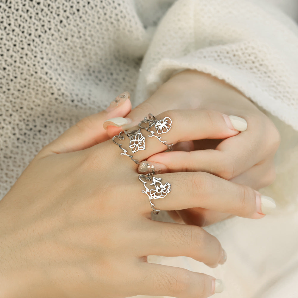 A stainless steel ring with a floral design, placed on a silky fabric surface.